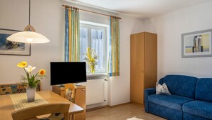A room with a dining table, a blue sofa, a TV, a wooden cabinet, and a window with curtains. - Farmhouse "Valtlhof - Apt 2" with Shared Pool, Shared Garden & Wi-Fi (Cornaiano)