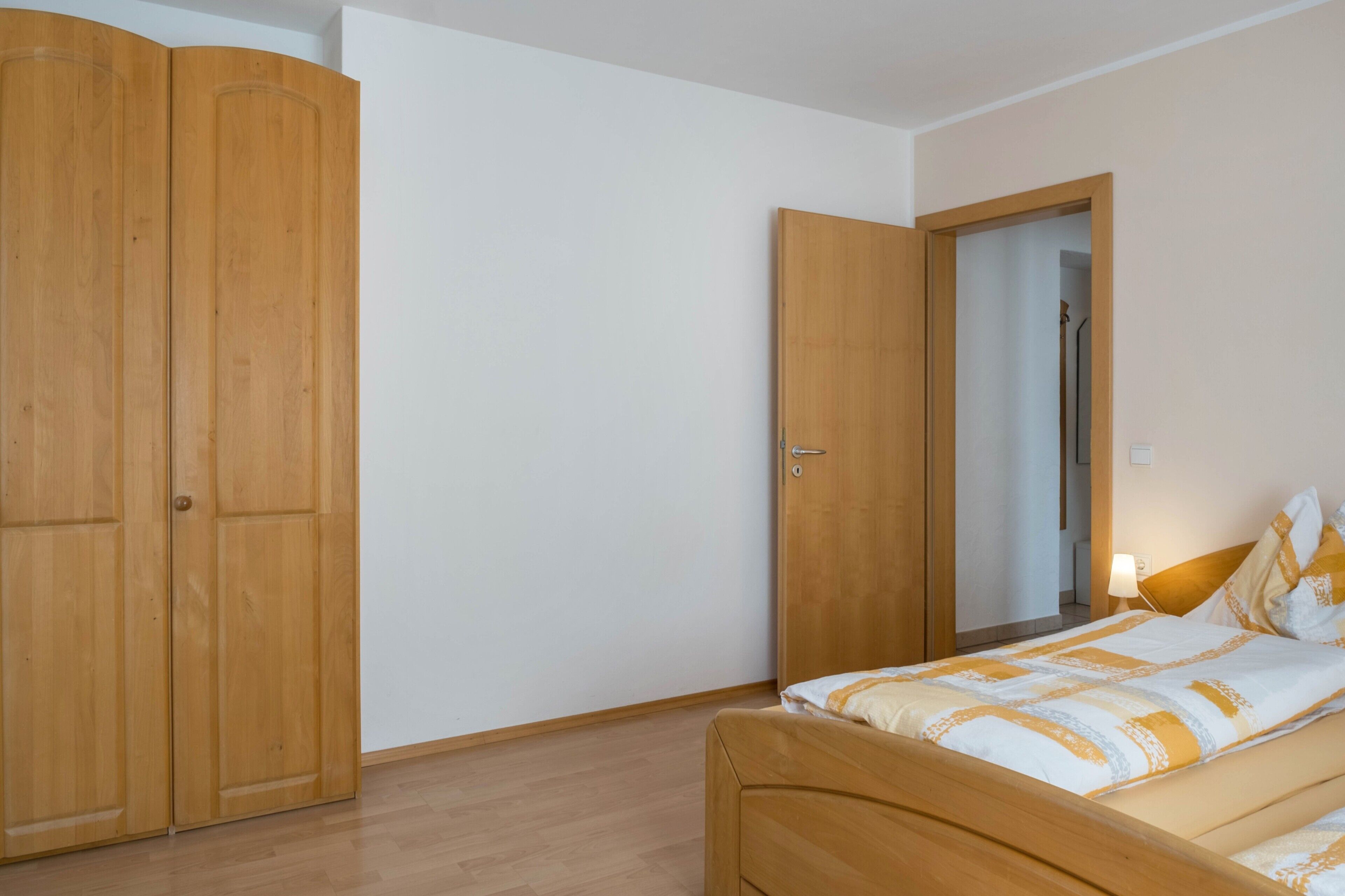 Ein Schlafzimmer mit einem Holzschrank, einem Bett mit gemustertem Überwurf und einer Tür zu einem weiteren Raum.