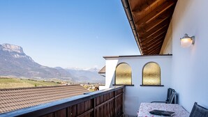 A balcony with a view of mountains, a table with chairs, and a wall-mounted light fixture. - Farmhouse "Valtlhof - Apt 1" with Shared Pool, Shared Garden & Wi-Fi (Cornaiano)