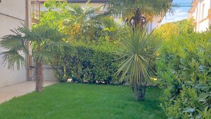 A well-maintained garden with a lawn, palm trees, and dense shrubbery. - Holiday Apartment 'Beba' with Private Garden and Wi-Fi (Lido di Jesolo)