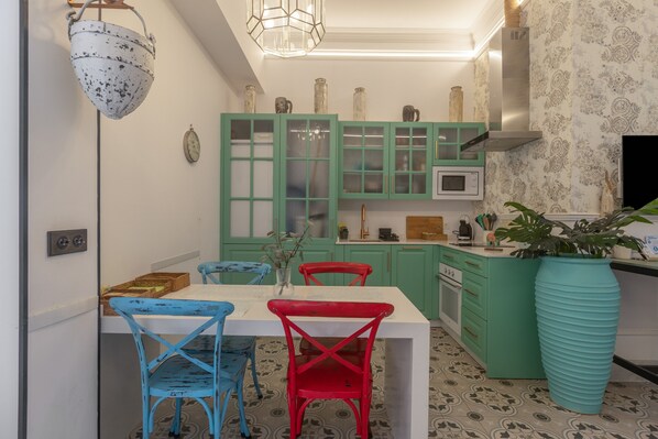 Une cuisine avec des meubles de couleur turquoise, un plan de travail blanc, un grand vase et un four à micro-ondes.