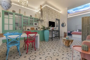 Une cuisine moderne avec des meubles de rangement verts, une table à manger avec des chaises bleues et rouges, et un grand vase.