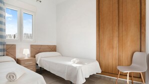 A bedroom with two beds, a wooden wardrobe, a chair, and a window with a view. - Holiday Home "Villa Montenmedio - Paula" with Mountain View & Pool (El Soto)