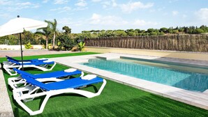 A swimming pool with blue lounge chairs and a white umbrella. - Holiday Home "Villa Montenmedio - Paula" with Mountain View & Pool (El Soto)