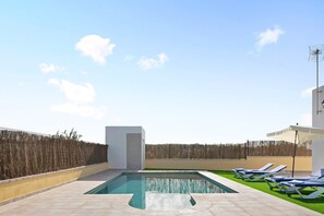 A swimming pool with lounge chairs, a white building, and a fence.