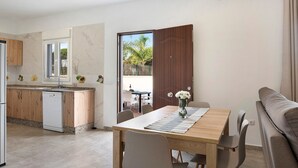 A modern kitchen with a dishwasher, a dining area with a wooden table and chairs, and a sofa. - Holiday Home "Villa Montenmedio - Paula" with Mountain View & Pool (El Soto)