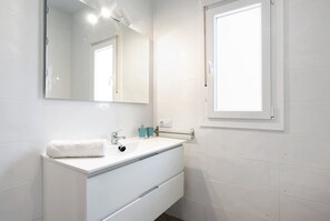 A bathroom with a white sink, mirror, and window.
