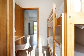 A narrow room with bunk beds, a white chair, and a wooden desk.