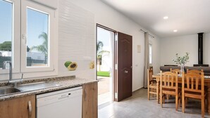 A modern kitchen with a dishwasher, a sink, and a dining area with wooden chairs and a table. - Pet-Friendly Holiday Home "Villa Montenmedio - Carmelo" with Mountain View & Pool (El Soto)