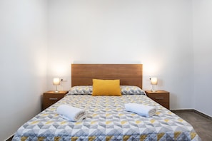 A neatly made bed with a geometric patterned bedspread, two bedside lamps, and a wooden headboard.