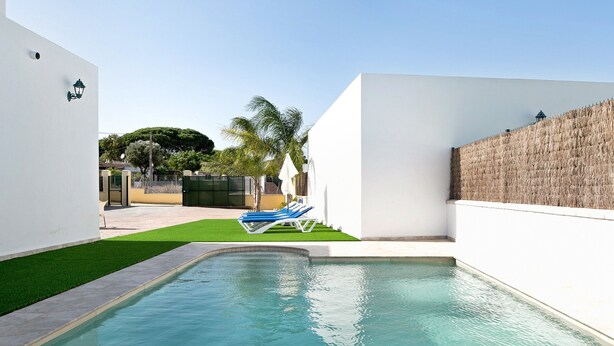 A swimming pool with a small deck area, a white wall, and a palm tree in the background. - Pet-Friendly Holiday Home "Villa Montenmedio - Carmelo" with Mountain View & Pool (El Soto)