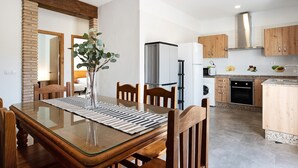 A dining area with a glass table, wooden chairs, and a vase with greenery. - Pet-Friendly Holiday Home "Villa Montenmedio - Carmelo" with Mountain View & Pool (El Soto)