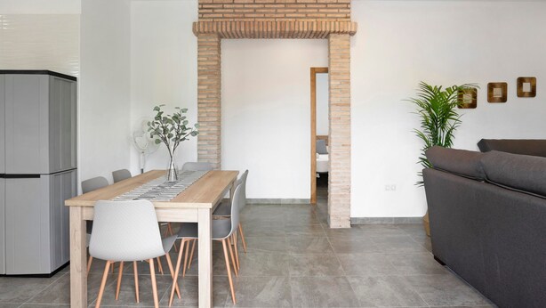 A modern kitchen with a dining table, chairs, and a brick archway leading to another room. - Holiday Home "Villa Montemedio - Paco" with Private Pool and Mountain View (El Soto)