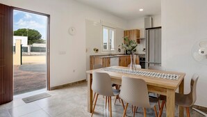 A modern kitchen with a dining area, wooden cabinets, a refrigerator, and a view through an open door. - Holiday Home "Villa Montemedio - Paco" with Private Pool and Mountain View (El Soto)
