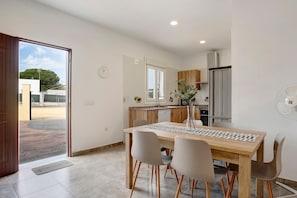 A modern kitchen with a dining area, wooden cabinets, a refrigerator, and a view through an open door.