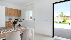 Une cuisine moderne avec des meubles en bois, un coin repas agrémenté d’un chemin de table à carreaux, et une vue sur un jardin par une porte vitrée.
