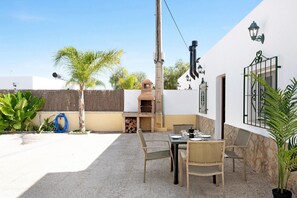 Une terrasse extérieure avec une table et des chaises, un barbecue et un tuyau d’arrosage bleu.