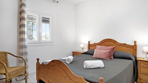 Une chambre à coucher avec un lit en bois, une chaise en osier, une table de chevet avec une lampe et une fenêtre avec des rideaux.