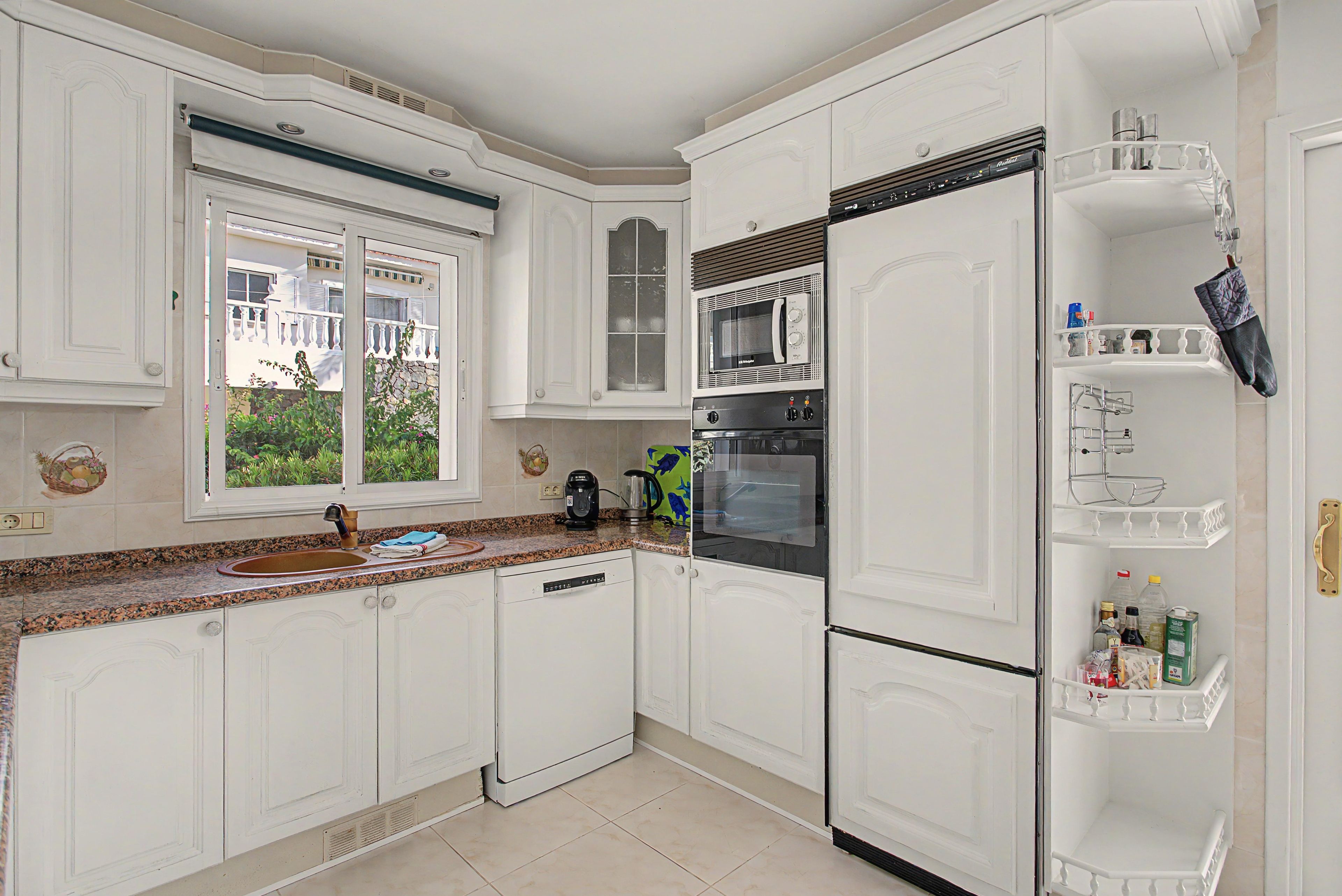 A kitchen with white cabinetry, a built-in oven, a refrigerator, and a window with a view of greenery outside.