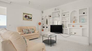 A living room with a sofa, a television, and a glass coffee table.