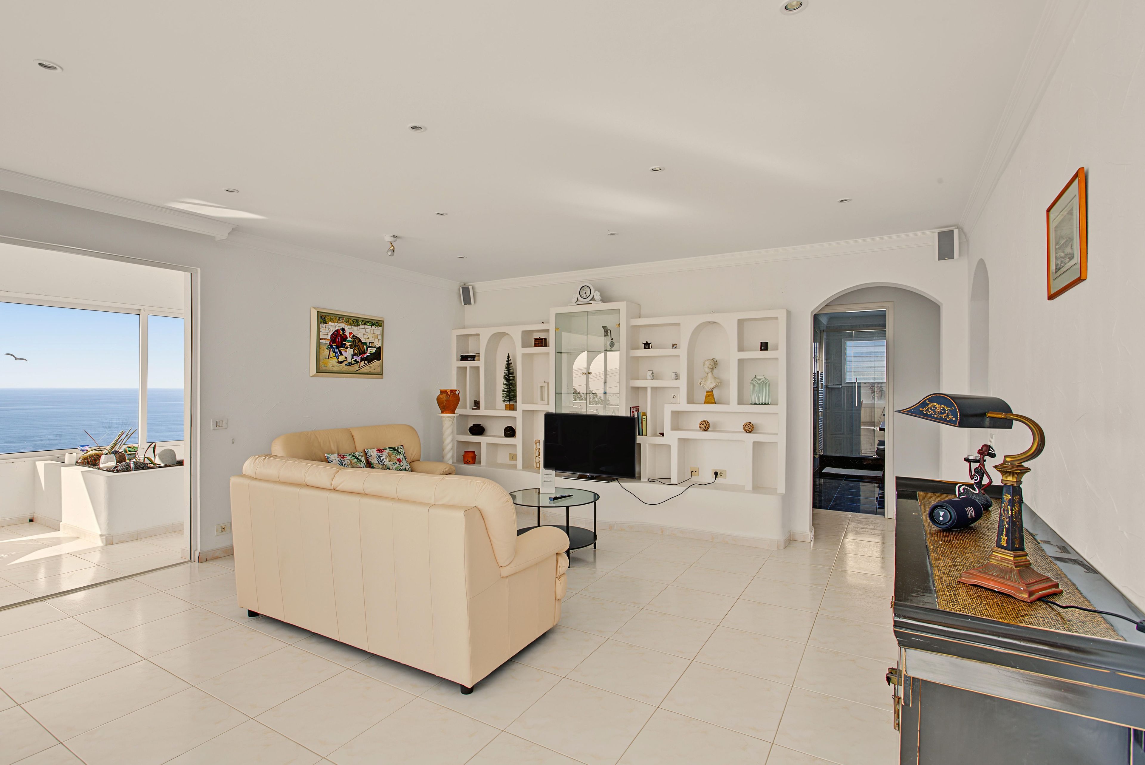 Un salon spacieux avec un canapé beige, un téléviseur à écran plat et une grande fenêtre donnant sur la mer.