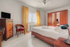 A hotel room with a bed, a wooden dresser, a chair, a television, and a ceiling fan.