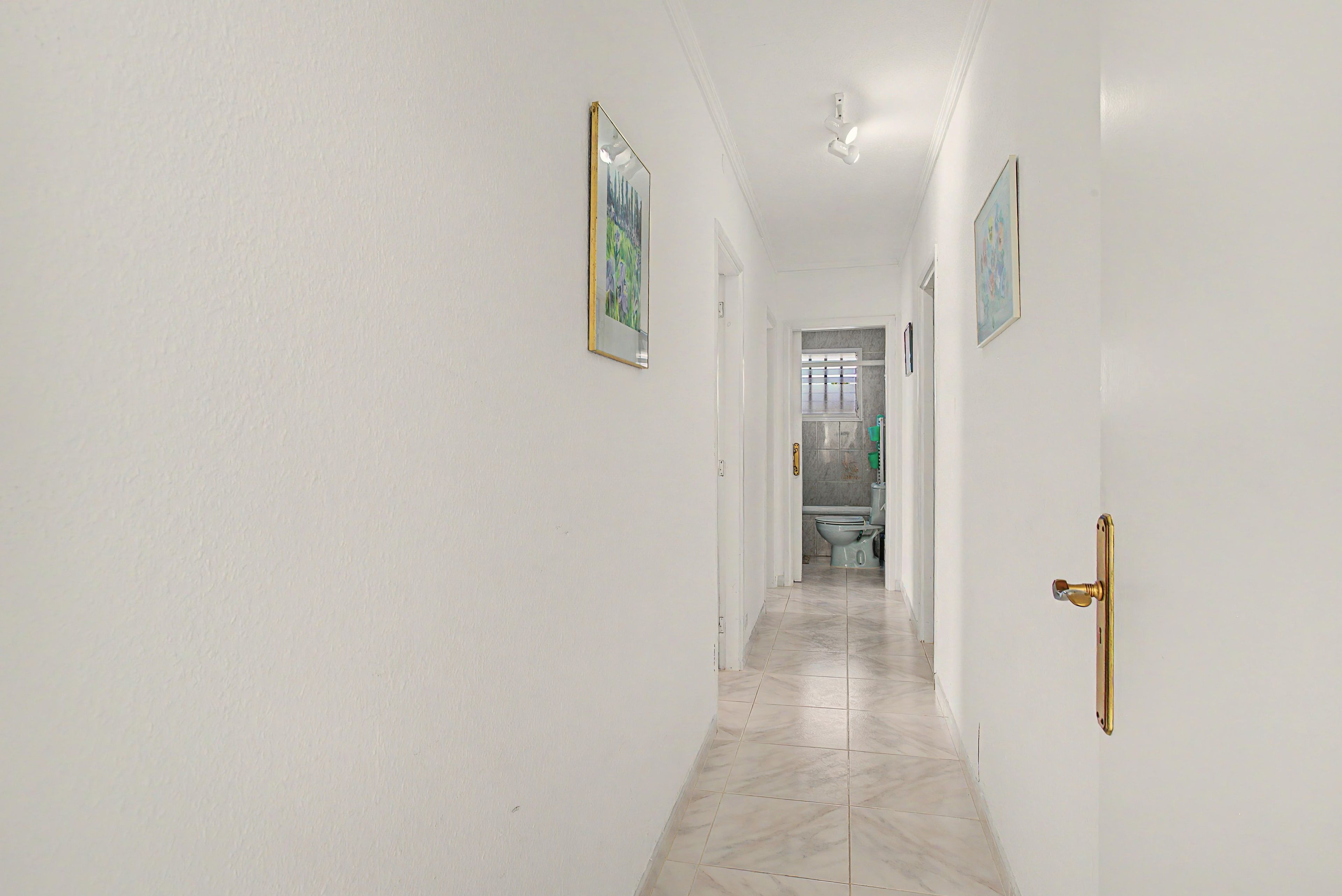 Un couloir aux murs blancs, doté d’un sol carrelé et d’une porte ornée d’une poignée dorée.