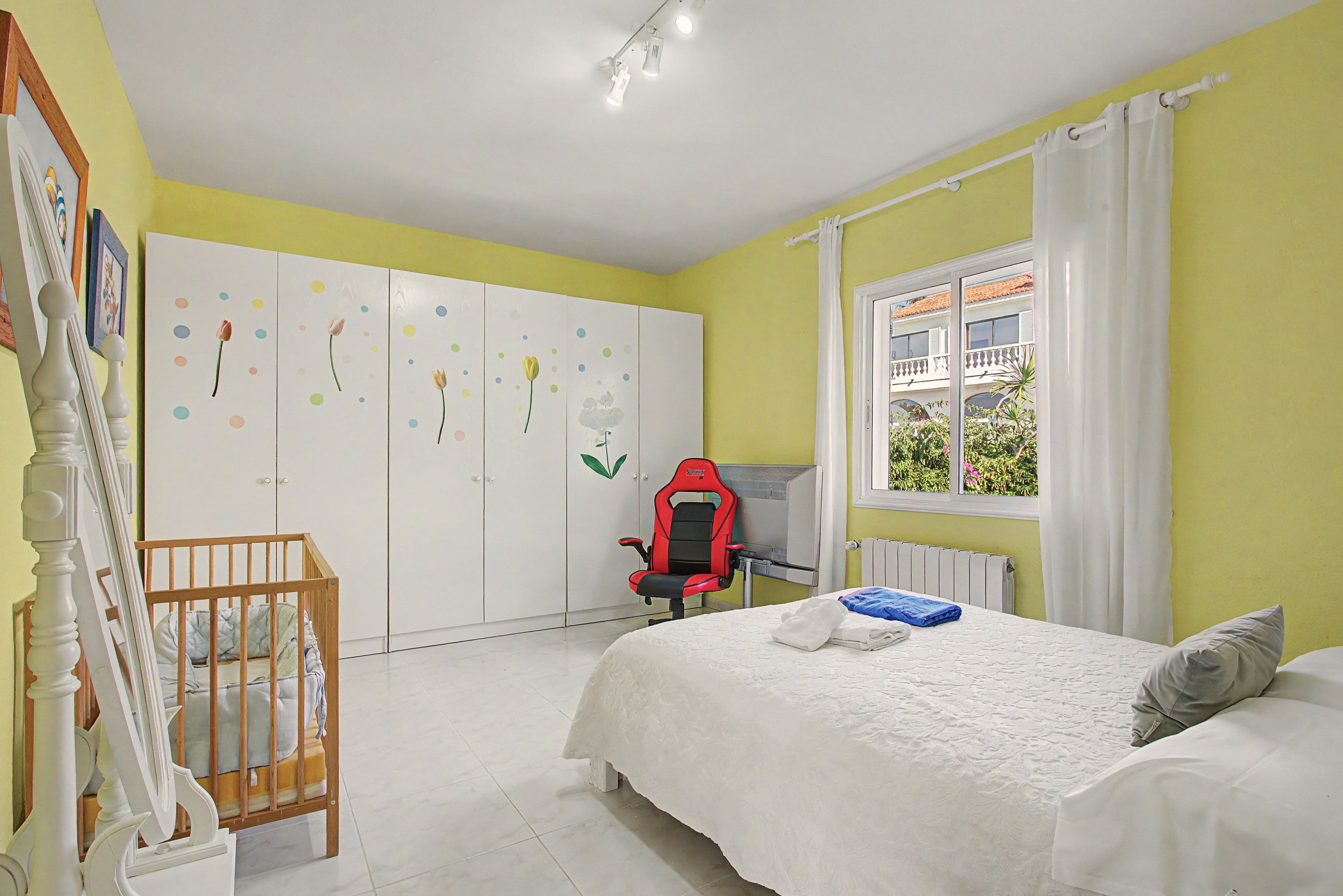 A bedroom with a bed, a desk, a chair, a wardrobe, and a window with curtains.