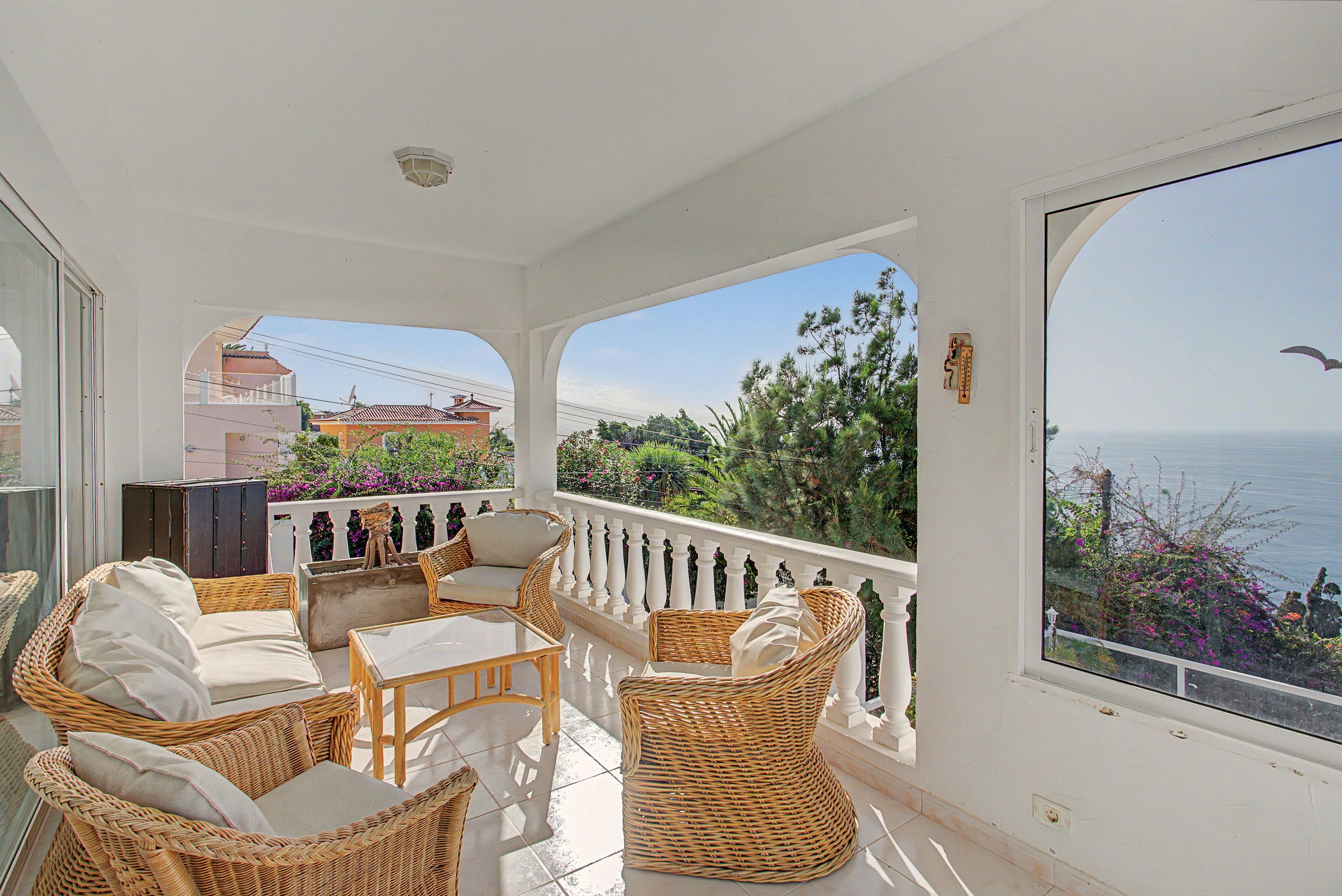 Ein Balkon mit Korbmöbeln, Blick auf das Meer und einem weißen Geländer.