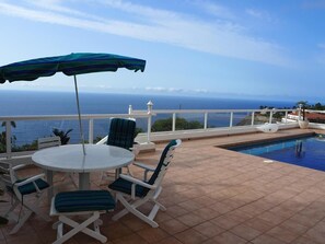 A terrace with a pool, a table, and chairs, overlooking a body of water. - Vacation Home "Hibiscus" with Sea View, Pool & Wi-Fi (santa ursula)