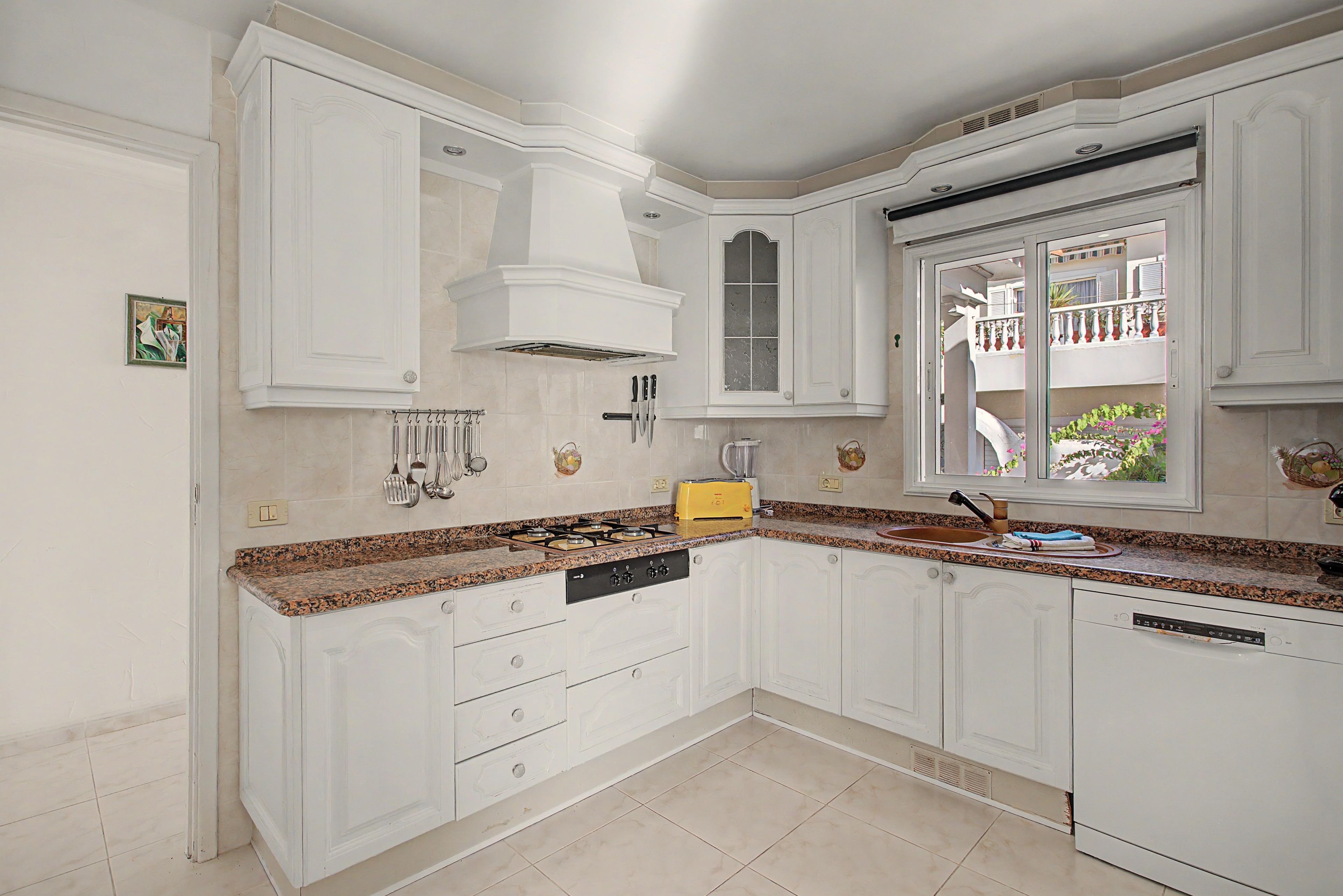 A kitchen with white cabinetry, a gas stove, and a window overlooking a balcony.