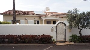 A residential house with a tiled roof, a satellite dish, a garage door, and a small garden with red-leafed plants. - Vacation Home "Hibiscus" with Sea View, Pool & Wi-Fi (santa ursula)