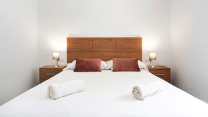 Un lit bien fait, avec une tête de lit en bois, deux tables de chevet avec des lampes et un mur blanc.
