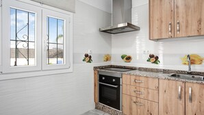 Une cuisine avec des carreaux blancs, une hotte en acier inoxydable, des armoires en bois, un four encastré et une fenêtre ornée de barreaux en fer décoratifs.