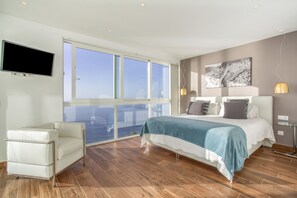 A modern bedroom with a large window, a bed with a blue and white bedspread, a white chair, and a mounted television. - Villa 'Crystal Ocean Villa' with Sea View, Heated Pool & Wi-Fi (EL SAUZAL)