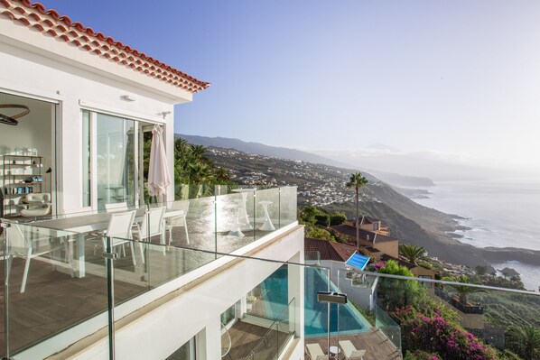 A modern building with a glass balcony overlooking a coastal landscape.