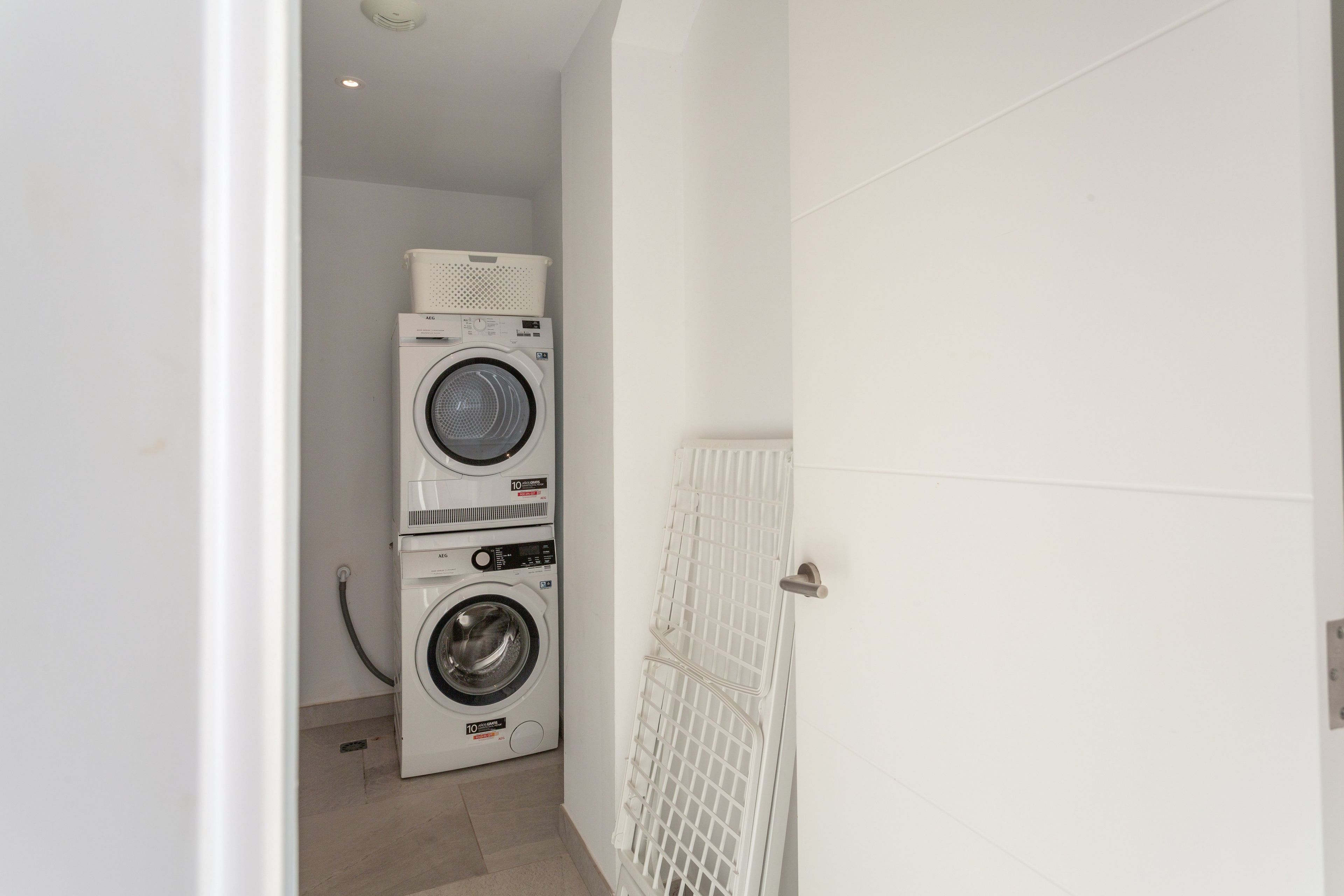 Una sala de lavandería con dos lavadoras apiladas y un tendedero.