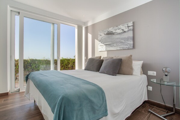 Un dormitorio moderno con una cama grande, una mesita de cristal y vistas al exterior.