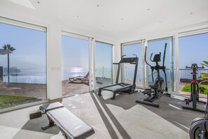 Un gimnasio con equipo de ejercicio y una banca, con vista a un cuerpo de agua.