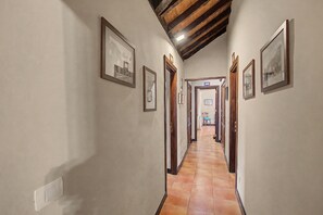 Un couloir aux murs ornés de tableaux encadrés, avec des portes en bois et un sol carrelé.