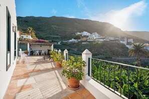 Una terraza con plantas en macetas, mobiliario exterior y vistas a un pueblo en la ladera.