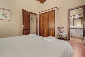 A bedroom with a bed, a chair, a wardrobe, and a bathroom visible through an open door. - Vacation Home "La Hacienda" with Sea View, Private Terrace & Wi-Fi (GARACHICO)