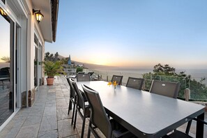 An outdoor patio with a table and chairs, a potted plant, and a view of the ocean.