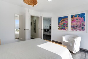 A bedroom with a large bed, a white chair, and two colorful paintings on the wall. - Vacation Home "Villa Bahía de Michel" with Sea View, Pool, Garden & Wi-Fi (santa ursula)