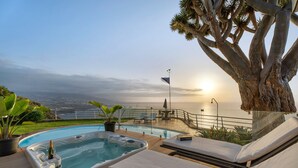 A pool area with lounge chairs, a hot tub, and a view of the ocean at sunset. - Vacation Home "Villa Bahía de Michel" with Sea View, Pool, Garden & Wi-Fi (santa ursula)