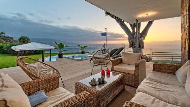 A covered outdoor seating area with wicker furniture, a pool, and a view of the ocean at sunset. - Vacation Home "Villa Bahía de Michel" with Sea View, Pool, Garden & Wi-Fi (santa ursula)