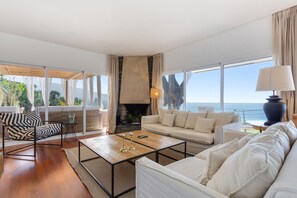 A modern living room with a sofa, armchair, and coffee table, a fireplace, and a view of the ocean. - Vacation Home "Villa Bahía de Michel" with Sea View, Pool, Garden & Wi-Fi (santa ursula)
