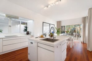 Une cuisine moderne avec des meubles blancs, un îlot central doté d’un évier et un coin repas comprenant une table et des chaises.