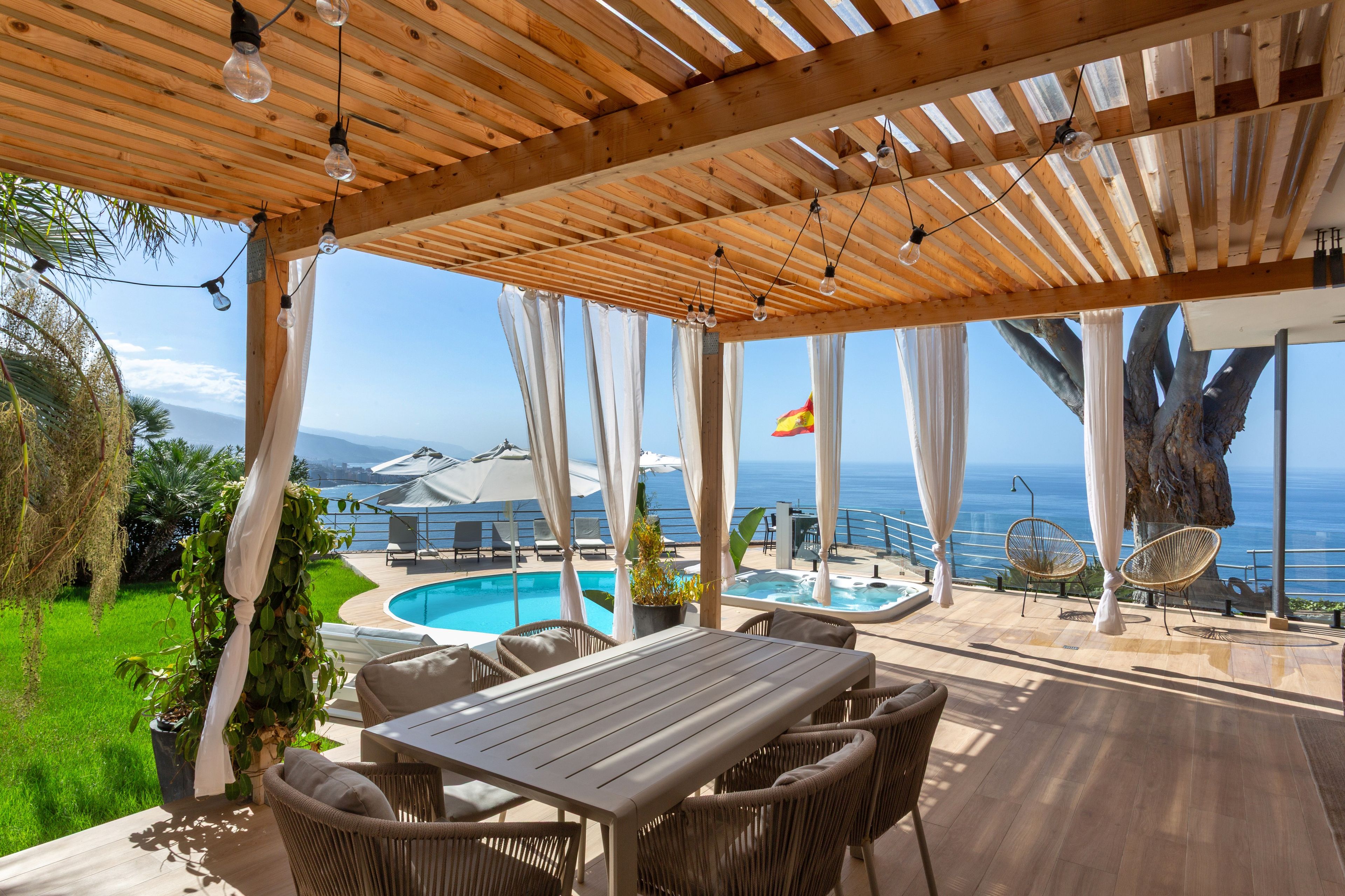 Un espacio al aire libre techado con piscina, mobiliario y vista al mar.