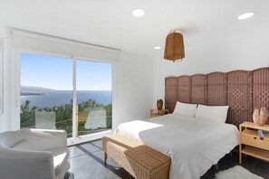 A bedroom with a large bed, a nightstand, a wicker bench, and a view of the sea. - Vacation Home "Villa Bahía de Michel" with Sea View, Pool, Garden & Wi-Fi (santa ursula)